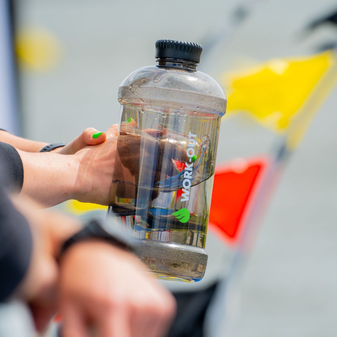 Gevulde Work-Out herbruikbare zwarte drinkbus van 2 liter met logo, vastgehouden door sportieve dame